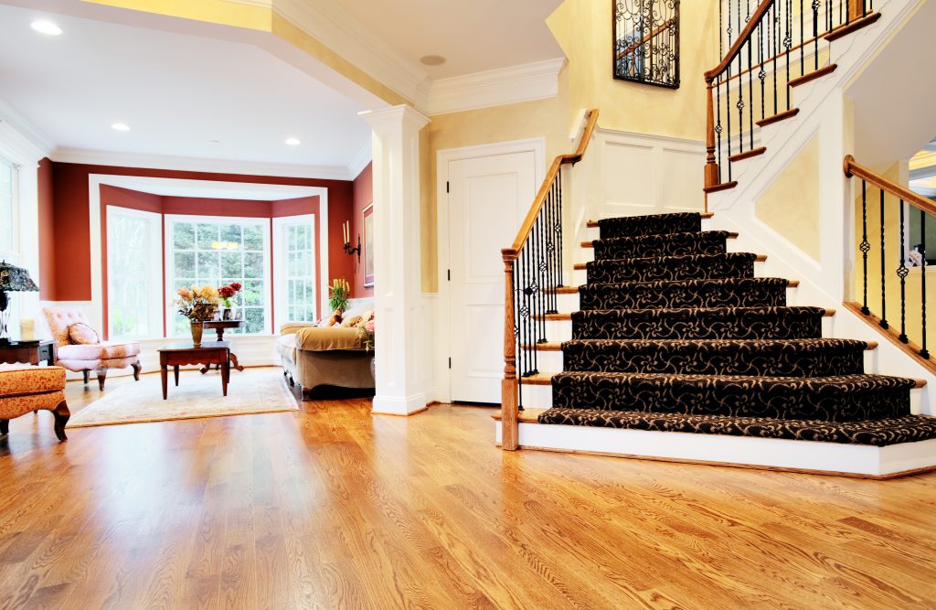 Open entryway with wood floor and staircase, with view of living room. Horizontal format.